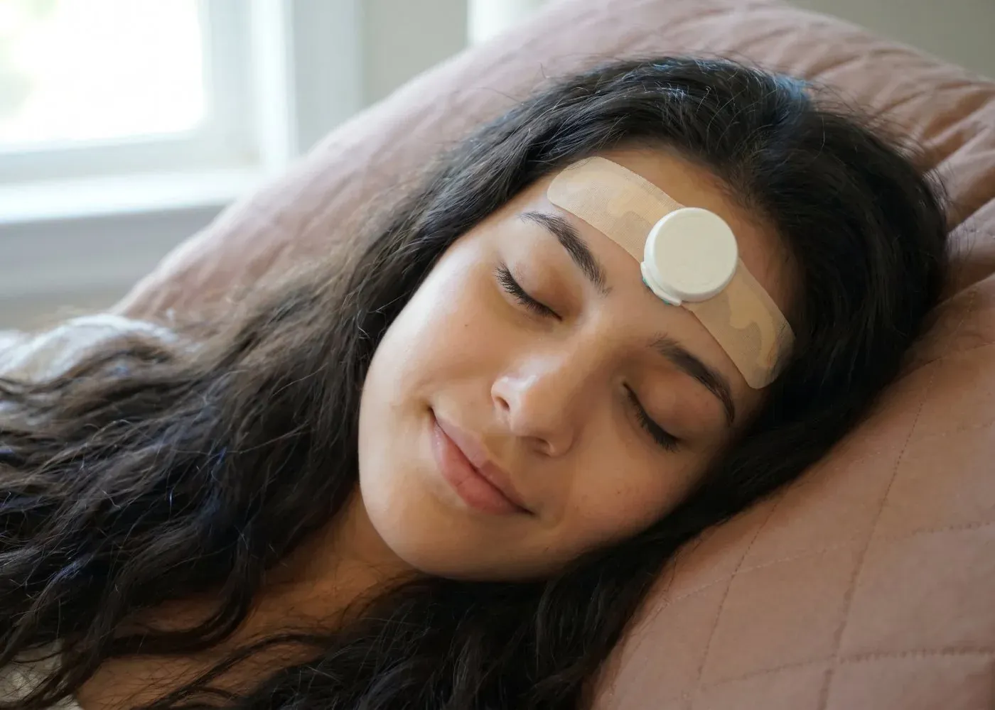 A woman asleep in bed wearing the JawSense sensor on her forehead